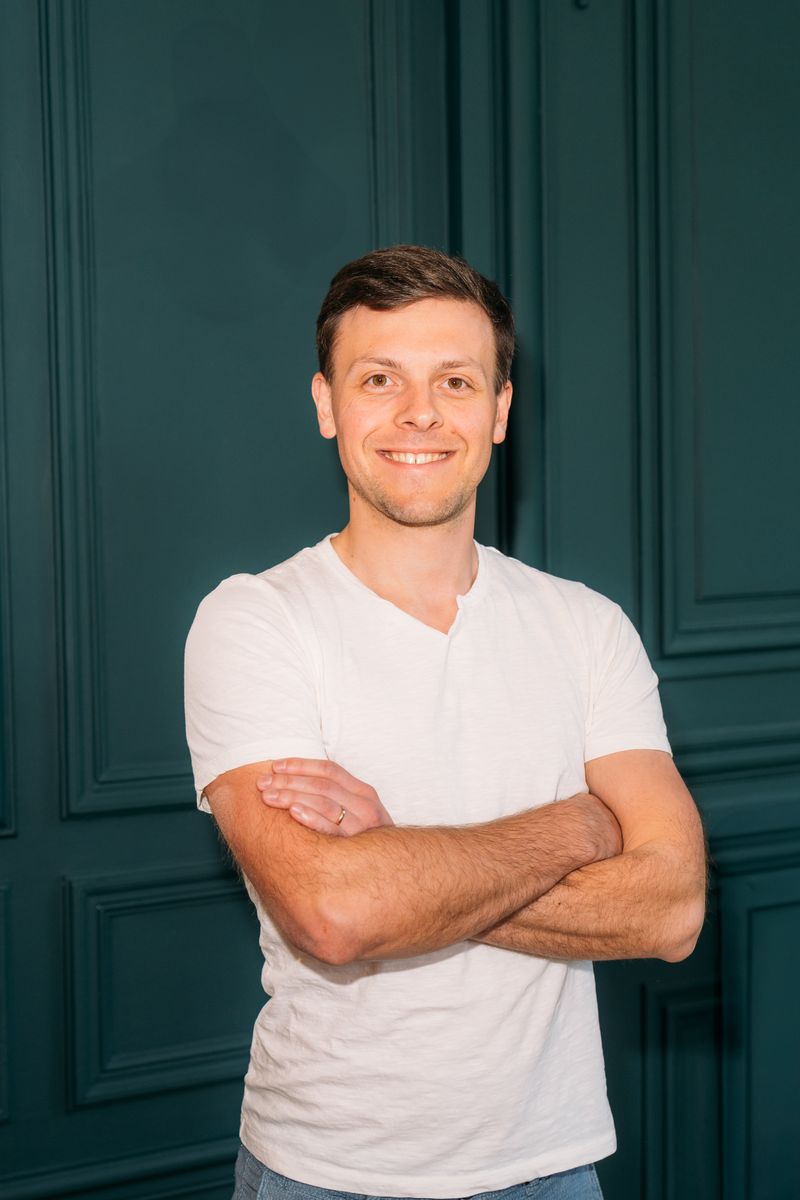 Portrait of Lukáš Mladý, smiling with arms crossed against a teal paneled wall